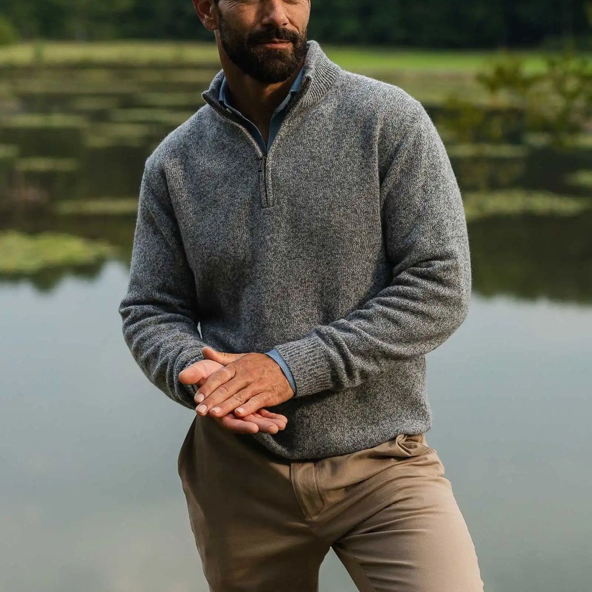 Man standing in an outdoor setting wearing a men's half zip sweater in heathered grey