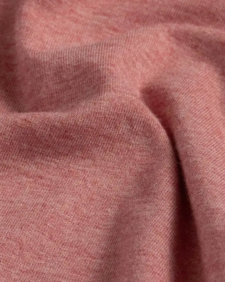 A close-up of draped heathered light red fabric showing its soft texture and fine knit detail.