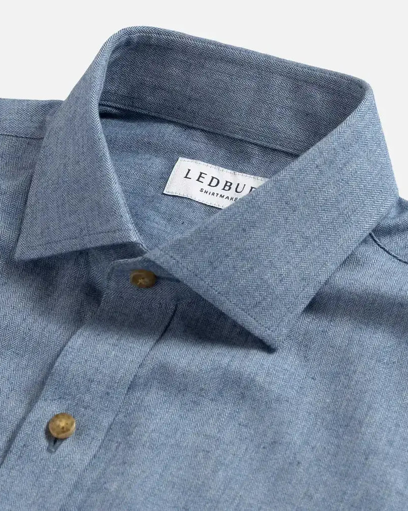 Close-up of a blue herringbone shirt collar with a Ledbury label on a light gray background