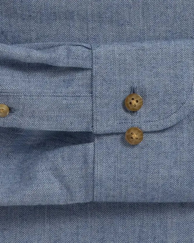 Close-up of a blue herringbone textured shirt cuff with buttons visible