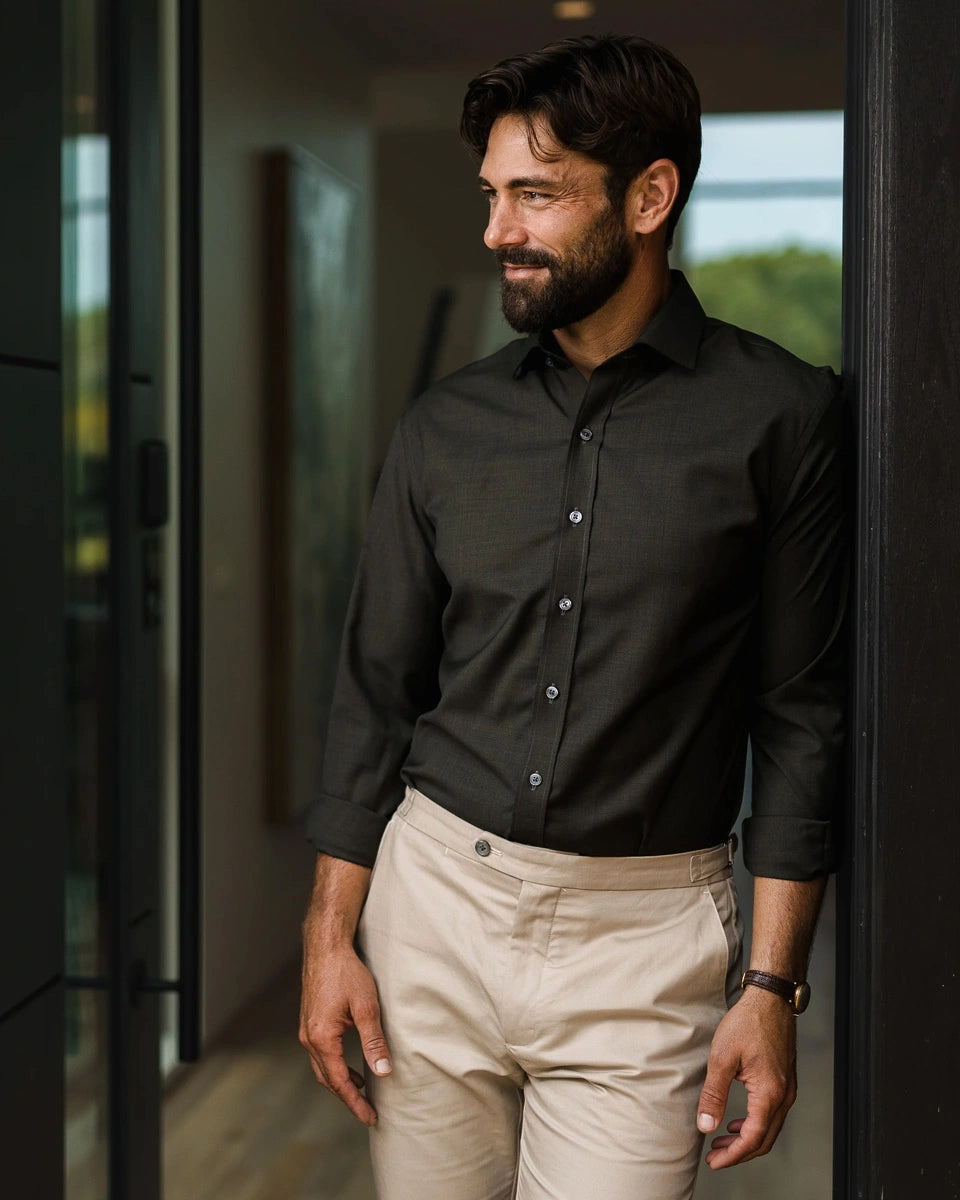 A man wearing a dark green long-sleeve fine Merino button-down shirt and beige trousers, standing in a doorway.