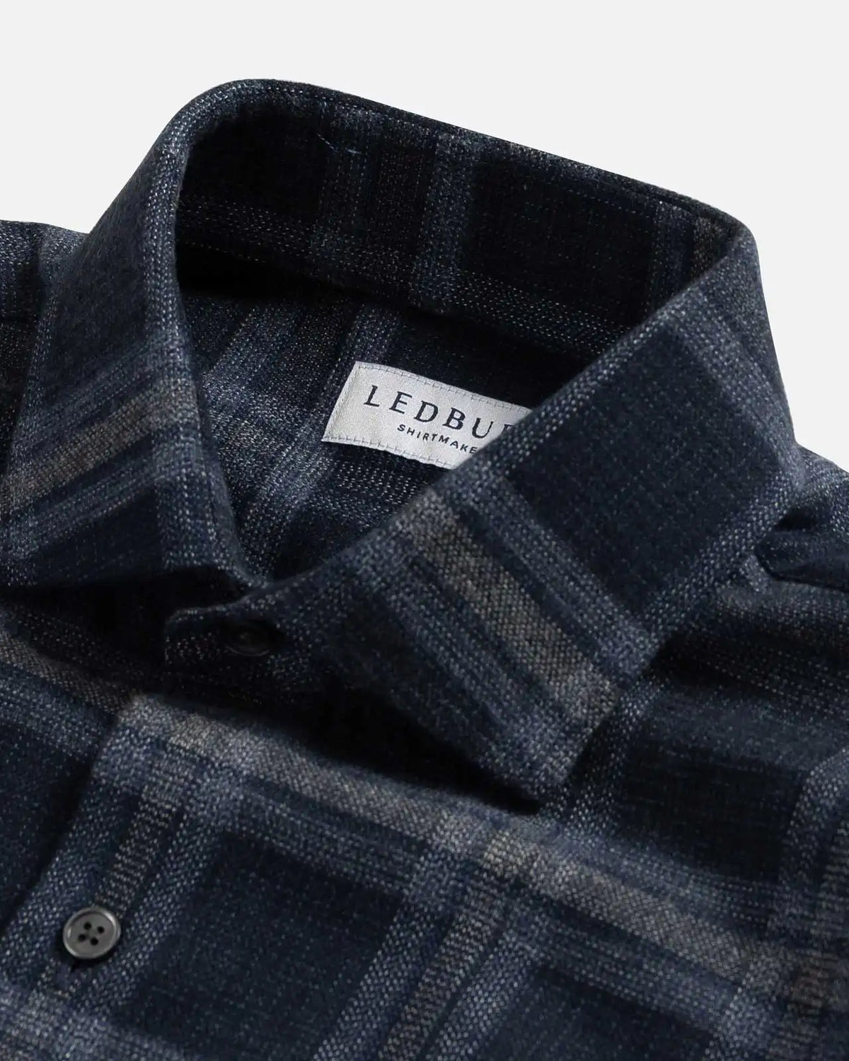 Close-up of a dark blue plaid shirt with a brand label on a white background