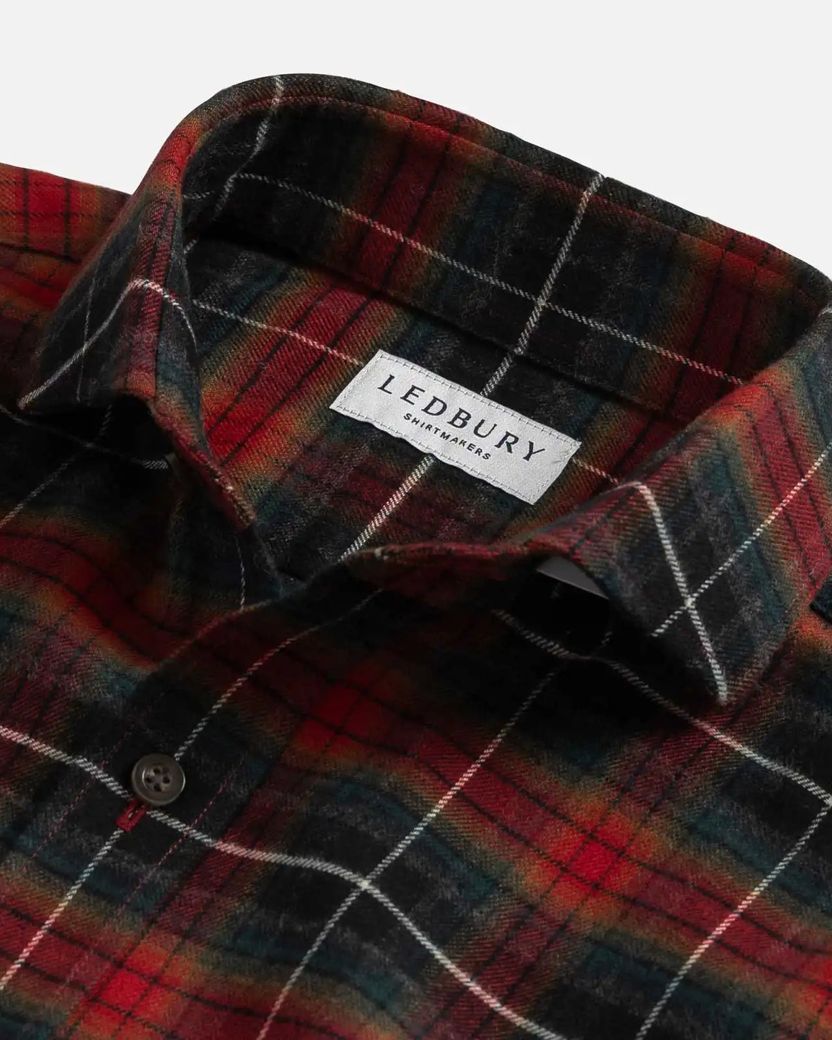 Close-up of a Ledbury plaid shirt in red, black, and green with white windowpane lines, showing the collar and button.