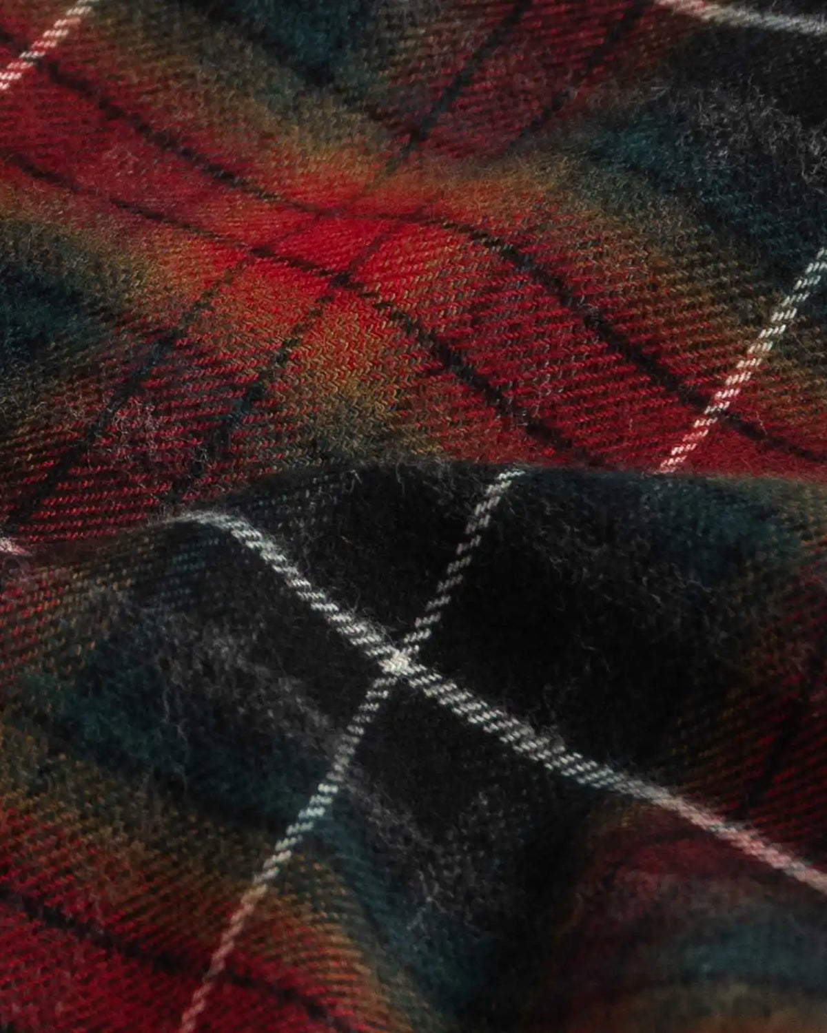A close-up of a plaid fabric with a tartan pattern in red, black, and green, accented by thin white diagonal stripes.