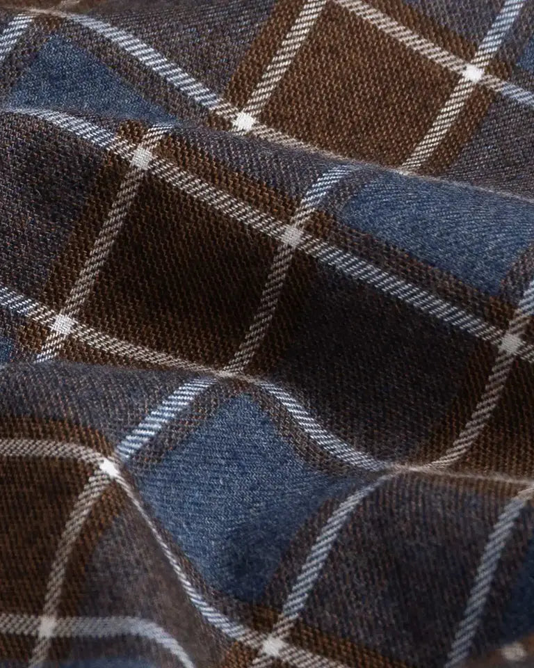 A close-up of a plaid fabric with a blue and brown checkered pattern, accented by thin white diagonal stripes.