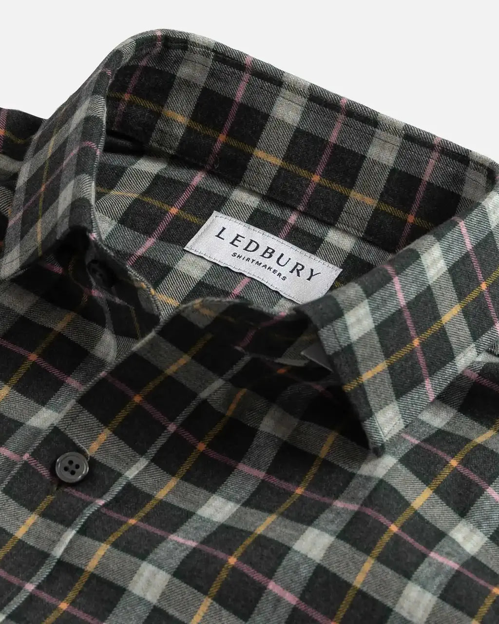 Close-up of a plaid button-down shirt collar with a visible LEDBURY label. The fabric has a dark charcoal base with intersecting gray, white, yellow, and pink plaid lines.