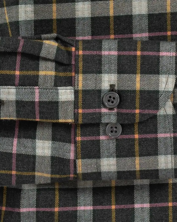 Close-up of a plaid button-up shirt fabric with a dark charcoal base, white and gray checks, and thin yellow and pink stripes. The shirt features a chest pocket with two dark buttons and a matching buttoned cuff.
