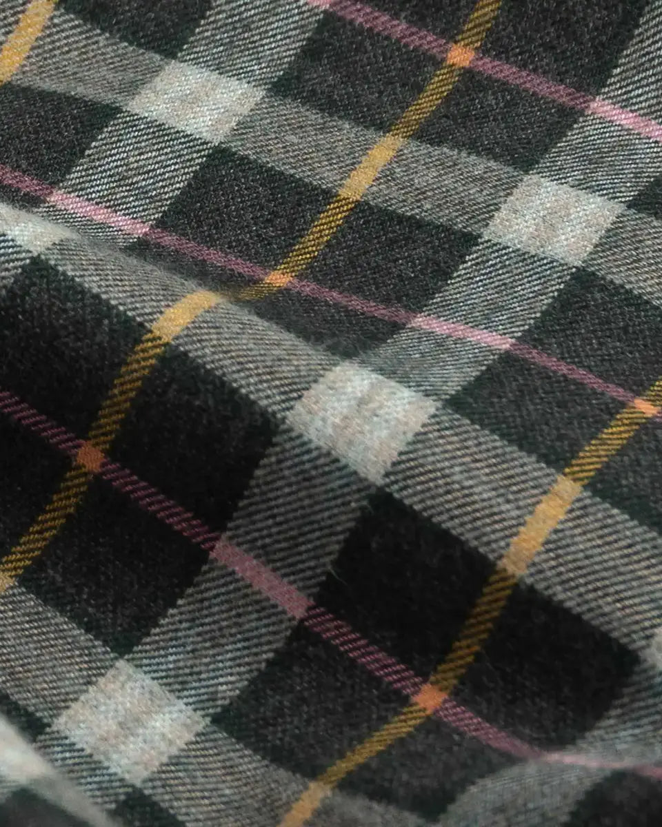 A close-up of a plaid fabric with a black, gray, and white tartan pattern accented by thin yellow and pink stripes.