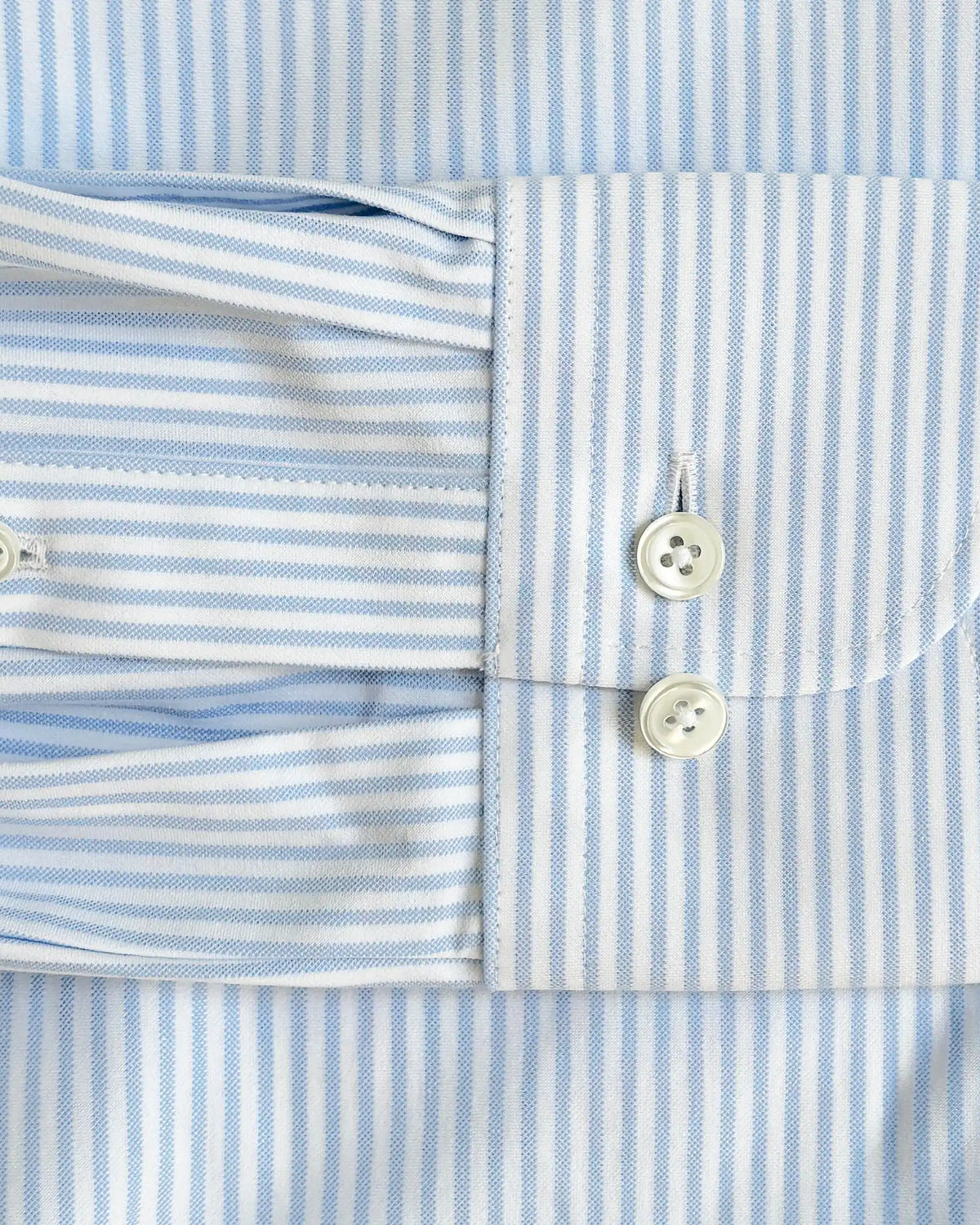 Close-up of a light blue and white striped dress shirt cuff with two white buttons, showing the fabric texture and pattern details.