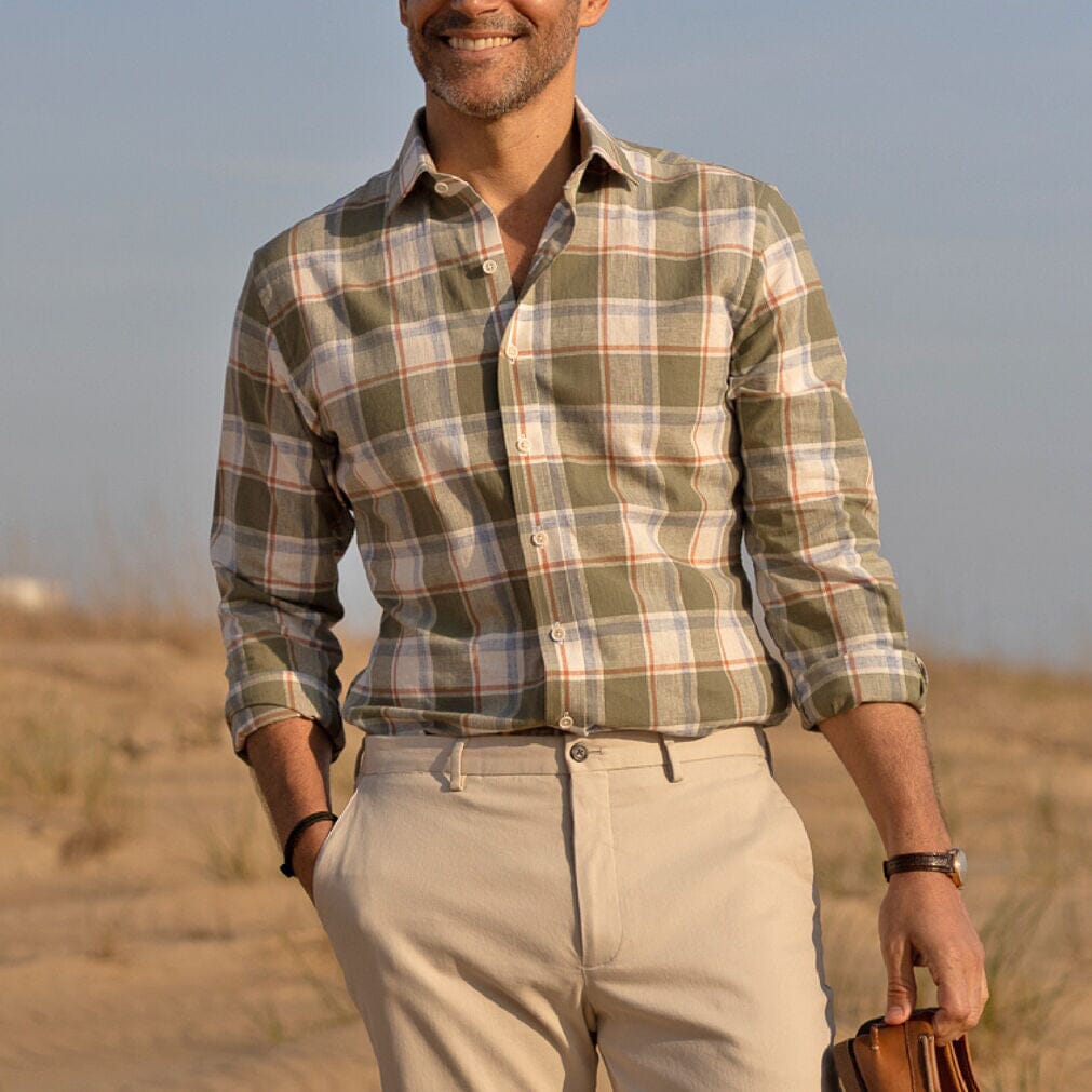Man wearing a plaid shirt and beige pants standing on the beach