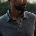 Close-up of a man wearing a textured gray knit polo neck sweater outdoors, with a blurred natural background.