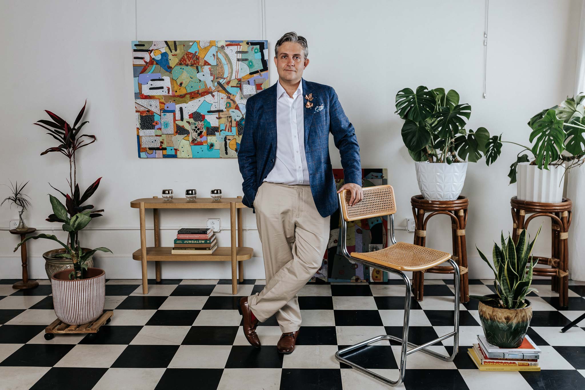 Man in a suit standing in a room with checkered floor, plants, and colorful wall art.