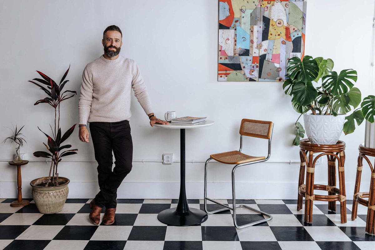 Man standing in a modern cafe with checkered floor, plants, and colorful wall art.