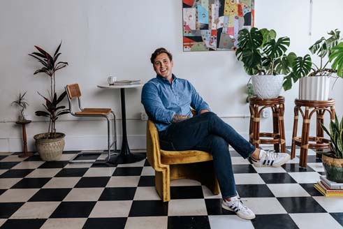 Man sitting on a yellow chair in a room with plants and checkered floor