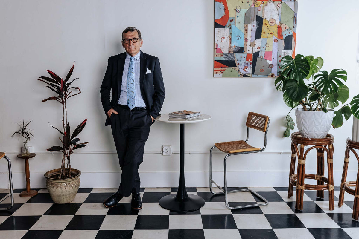 Man in a suit standing in a stylish room with plants and a checkered floor.