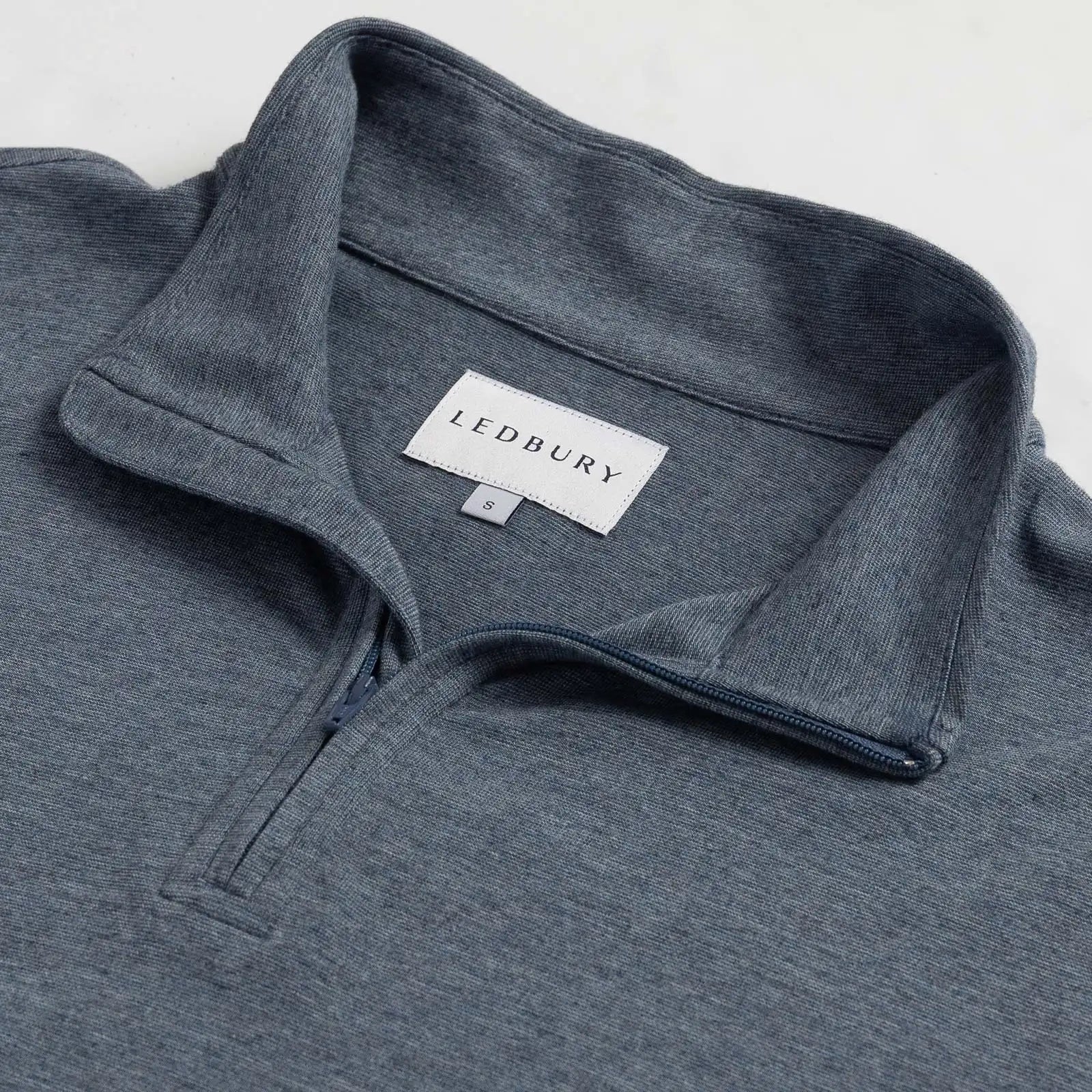 Close-up of a heather blue quarter-zip pullover sweater with a collar, showing the LEDBURY brand label inside the neck.