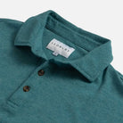 Close-up of a teal heathered polo shirt collar with brown buttons and a visible LEDBURY neck label on a light gray background.