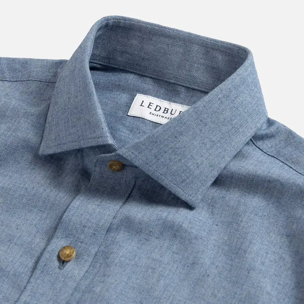 Close-up of a blue herringbone shirt collar with a Ledbury label on a light gray background