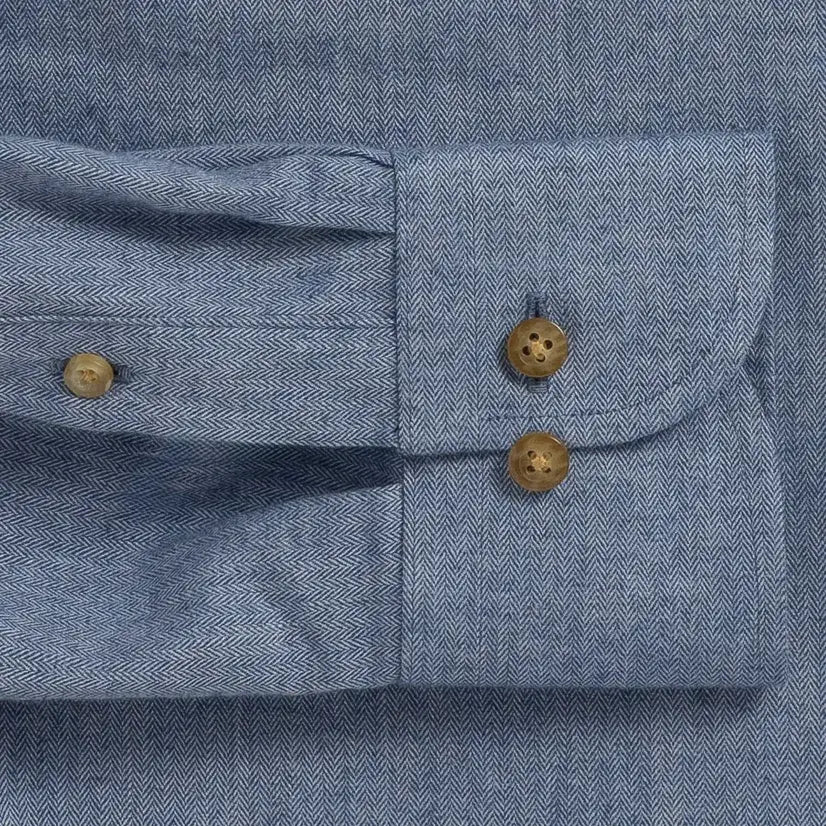 Close-up of a blue herringbone textured shirt cuff with buttons visible