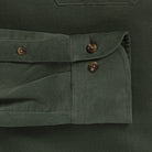 Close-up detail of an olive green corduroy shirt pocket with buttoned flap and dark brown buttons.