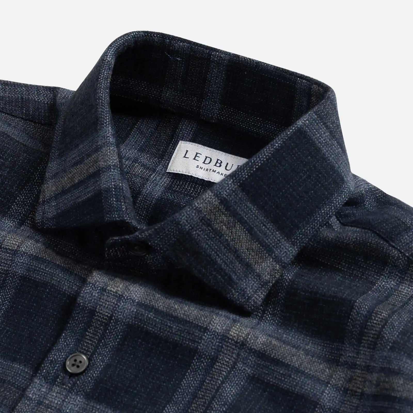 Close-up of a dark blue plaid shirt with a brand label on a white background