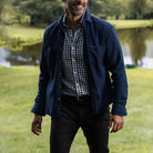 Man wearing a the blue Lisden utility shirt and checkered shirt standing in a park with a lake in the background