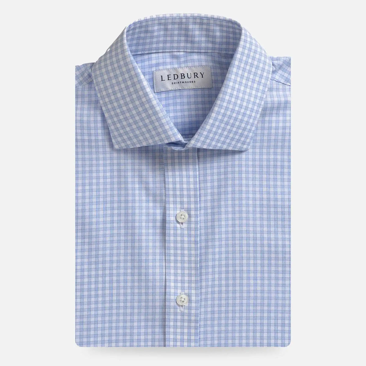 A folded light blue and white gingham dress shirt by Ledbury, featuring a classic collar, white buttons, and a clean white background.