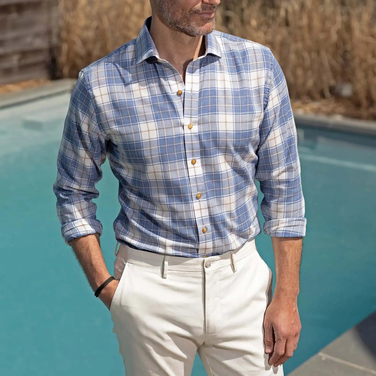 Man wearing a blue plaid shirt and white pants by a pool