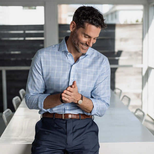 Man wearing a light blue checkered shirt and dark pants in a modern room.
