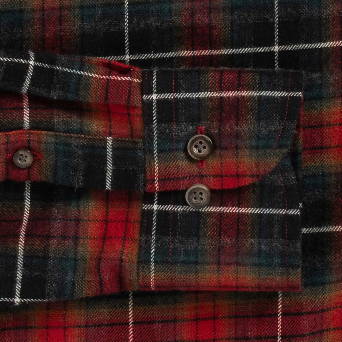 Close-up of a red and black plaid flannel shirt cuff with two buttons and white stripe lines.