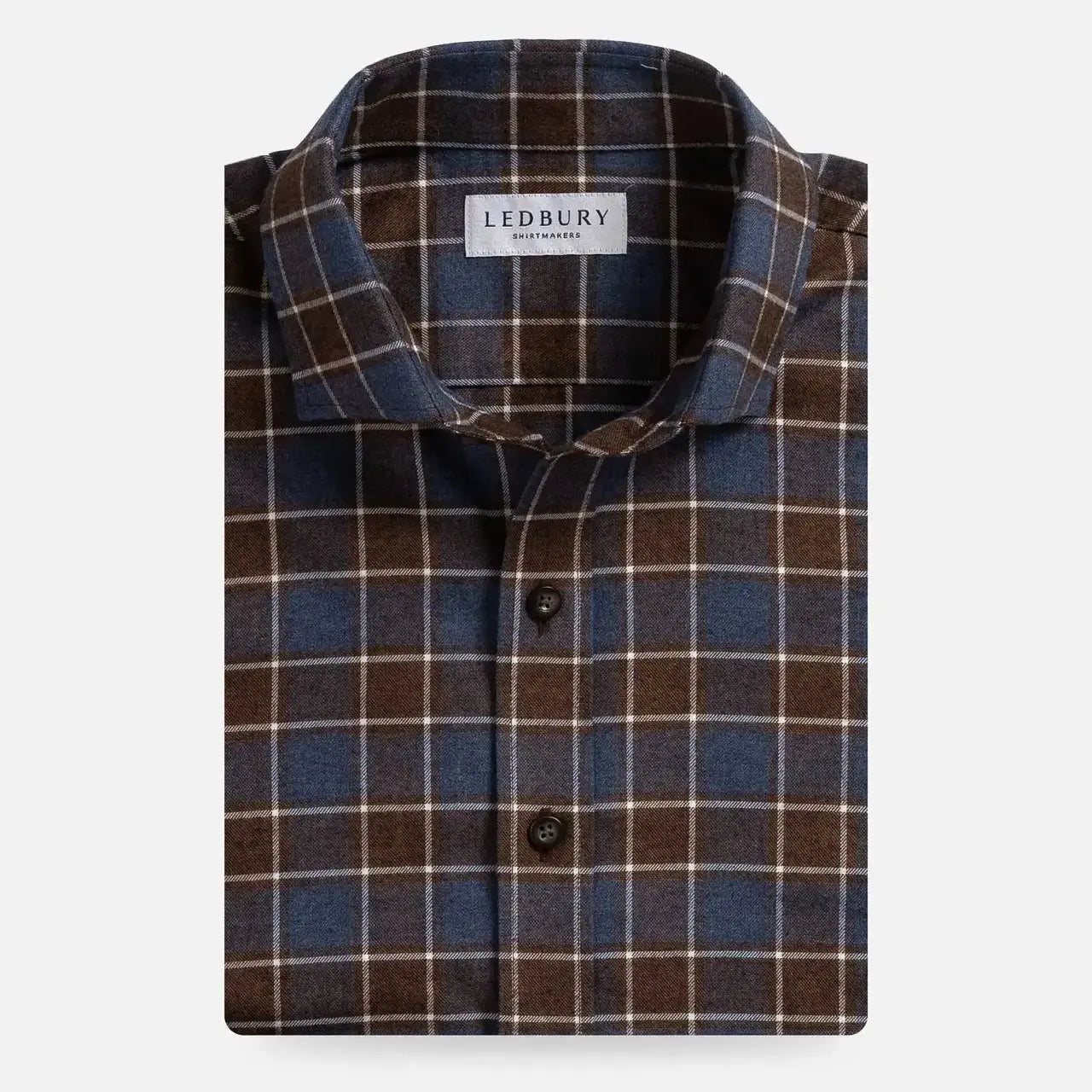 A folded men's button-up shirt by Ledbury, featuring a classic plaid pattern in dark brown, slate blue, and thin cream stripes, set against a plain light gray background.