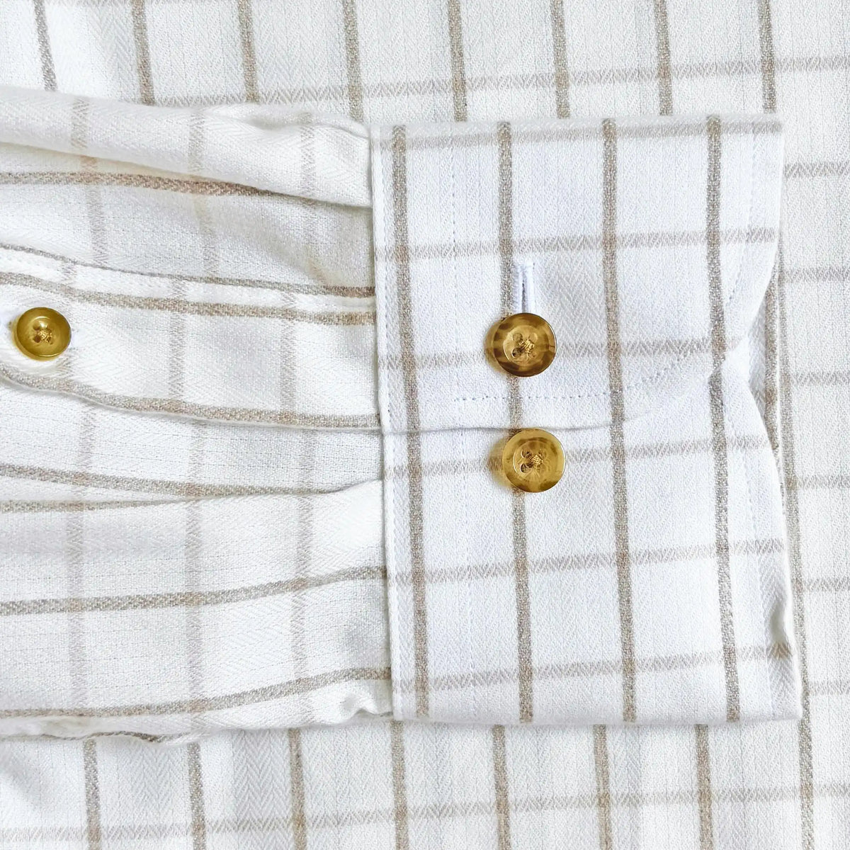 Close-up of a white and beige windowpane plaid shirt showing the buttoned cuff with gold-toned buttons.