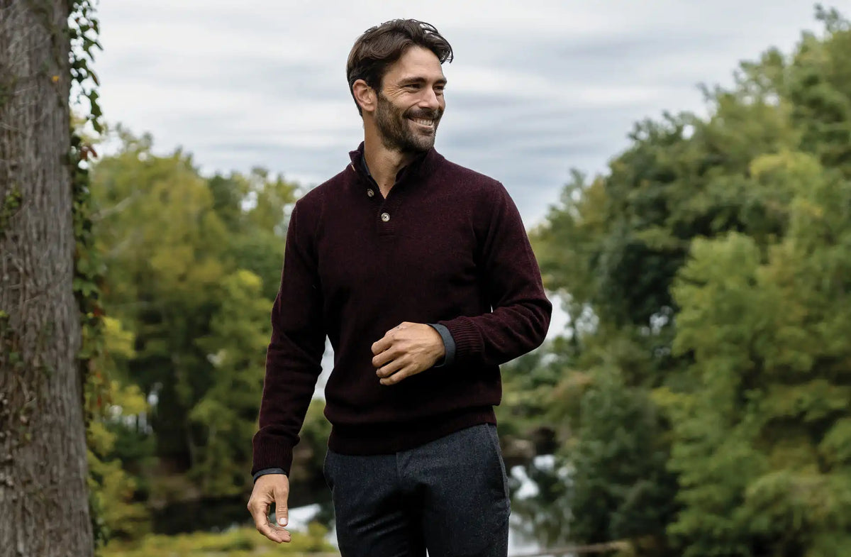 Man wearing a dark red sweater walking outdoors with trees in the background