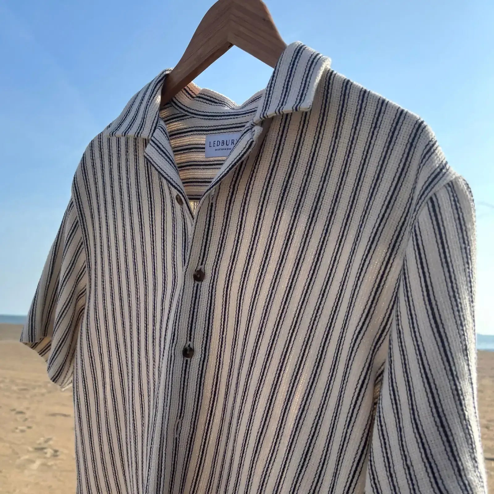 Ledbury navy and cream striped camp collar shirt hanging on a hanger at the beach