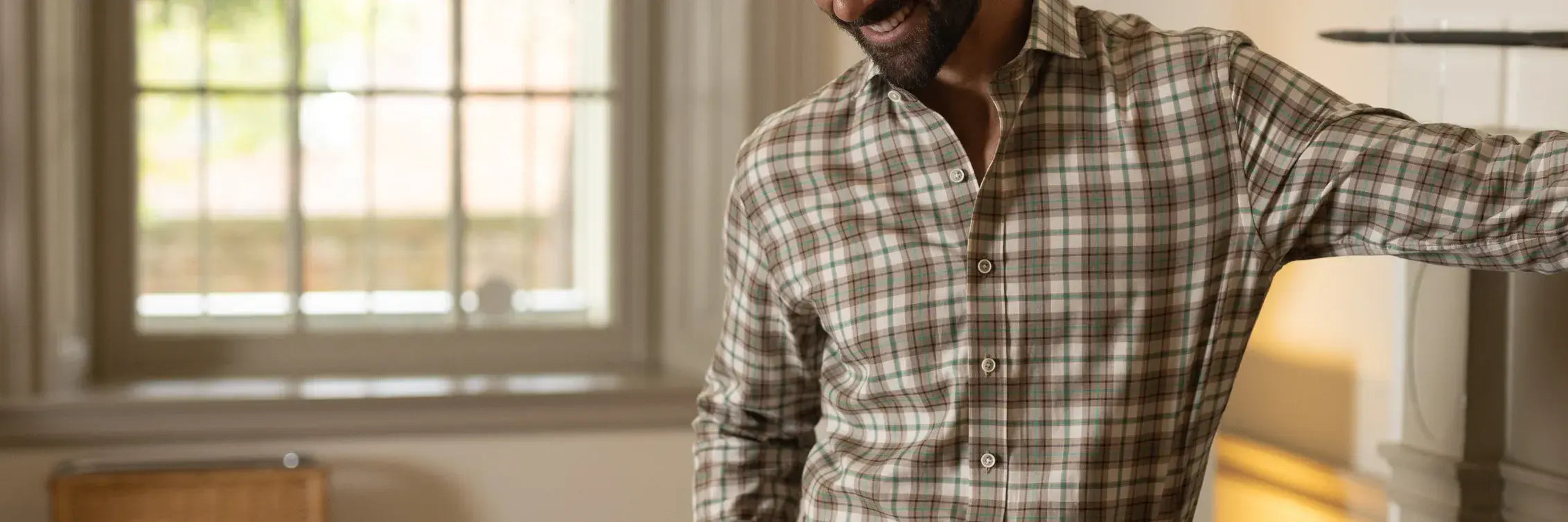 Man wearing a plaid shirt standing in a room with a window in the background