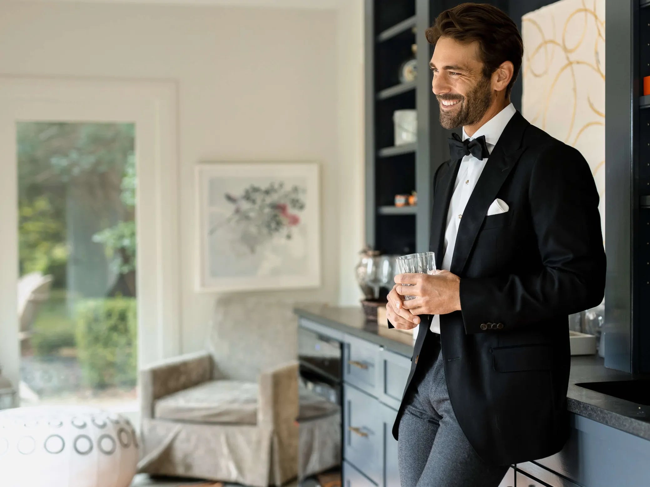 Male model wearing a tuxedo shirt and black jacket, holding a cocktail 