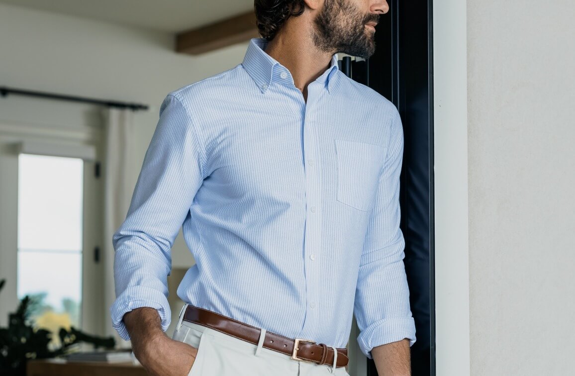 Model leaning up against a doorframe wearing a light blue and white striped Oxford shirt from Ledbury