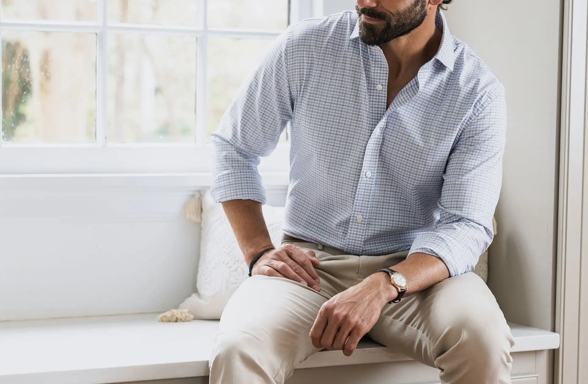 Man sitting on a white bench in a bright room wearing a checkered shirt and beige pants.