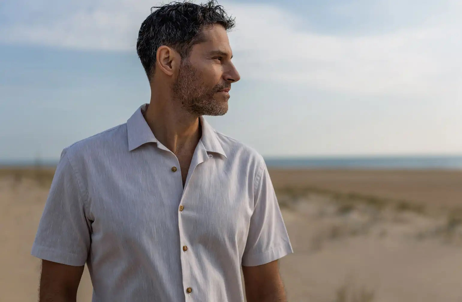 Man standing on a beach wearing a light-colored short sleeve shirt with a blurred background