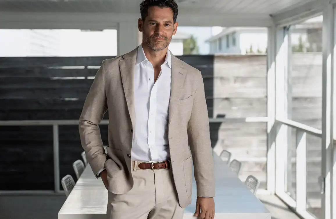 Man in a tan suit and white dress shirt standing in an outdoor setting