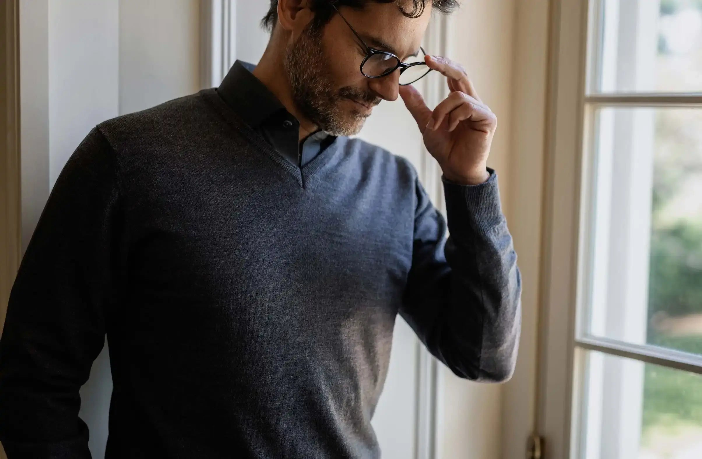 Man adjusting glasses indoors near a window